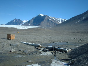 Field site in Antarctica with a crate in the foreground and steep mountains in background.